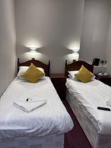 Hadleigh Hotel في إيستبورن: سريرين في غرفة الفندق مع شراشف بيضاء ومخدات صفراء