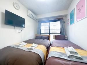 two beds in a room with a tv on the wall at nestay suite tokyo tabata in Tokyo