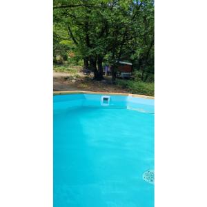 a blue swimming pool with a tree in the background at La roulotte rose rouge in Valgorge