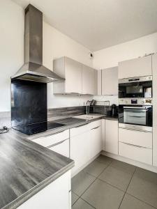 una cocina con armarios blancos y electrodomésticos de acero inoxidable en Grand Appartement Paris et Disneyland 4pers, en Neuilly-sur-Marne