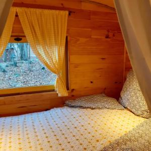 ein Schlafzimmer mit einem Bett mit einem Fenster und einem Vorhang in der Unterkunft Roulotte avec piscine la jonquille in Valgorge
