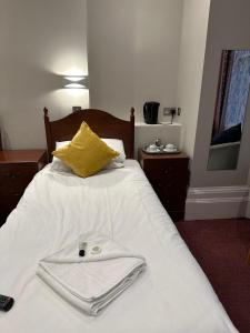 ein weißes Bett mit einem gelben Kissen und einem Bademantel darauf. in der Unterkunft Hadleigh Hotel in Eastbourne