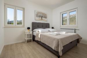 a white bedroom with a bed and two windows at Villa Big Garden in Primorski Dolac