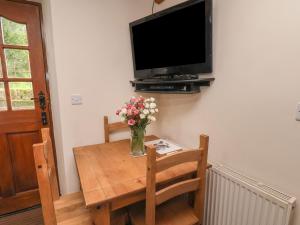 a vase of flowers on a wooden table with a television at Cow Byre Cottage in Whitby