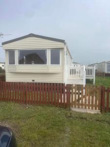 a small white house behind a wooden fence at 185 Holiday Resort Unity in Berrow