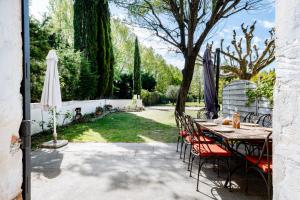 una mesa con sillas y una sombrilla en el patio en La Bastide des Joncquiers, en LʼIsle-sur-la-Sorgue