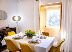 une table blanche avec des chaises jaunes et une fenêtre dans l'établissement Tio Zé - Casas de Selim, à Arcos de Valdevez
