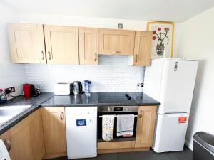 cocina con armarios de madera y nevera blanca en Lovely 2 bedroom flat with free parking, great transport links to Central London, the Excel Centre, Canary Wharf and the O2!, en Londres