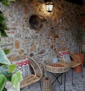 três cadeiras e uma mesa em frente a uma parede de pedra em Vila Delfina em Lousã