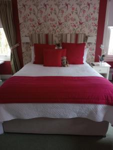a bed with red pillows and a cat sitting on it at Smiddy House in Spean Bridge
