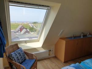 Zimmer im Dachgeschoss mit einem großen Fenster und einem Stuhl in der Unterkunft Ferienwohnung Inselblick Norddeich mit Meerblick in Norden