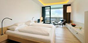 um quarto branco com uma cama grande e uma cadeira em Bio & Wellnesshotel Pazeider - Healing Garden above Meran em Marlengo