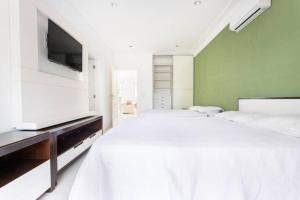 a white bedroom with a large bed and a flat screen tv at Suites Guarujá Pernambuco in Guarujá