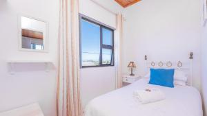 a white bedroom with a bed and a window at Suikerbekkie in Struisbaai