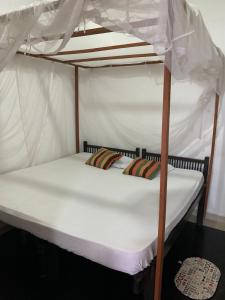 Litera con sábanas blancas y dosel en Surf Villa Hiriketiya en Matara