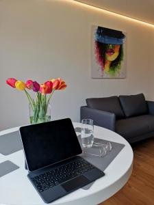 a laptop on a white table with flowers and a couch at Moderne Ferienwohnung Gartenblick in Amtzell