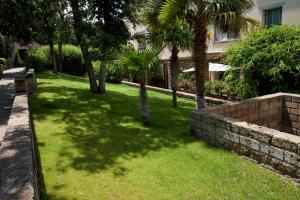 un patio verde con palmeras y una pared en Confortevole Bilocale Giardino Doppio Parcheggio, en Punta Ala