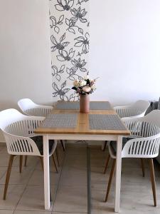 a table with white chairs and a vase with flowers at Ada Wellness Apartman Siófok in Siófok