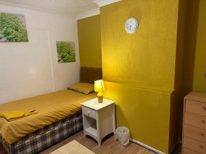 a yellow bedroom with a bed and a clock on a wall at Quick Stop Night Stay - Gatwick in Crawley