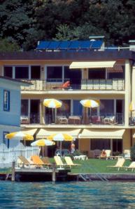 a hotel with chairs and umbrellas on the water at Seehaus Jamek in Pörtschach am Wörthersee