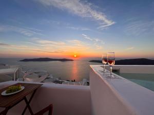 zwei Gläser Wein auf einem Balkon mit Sonnenuntergang in der Unterkunft Esmi Suites Santorini in Imerovigli
