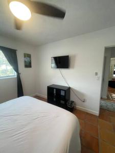 1 dormitorio con 1 cama blanca y TV de pantalla plana en Grotto pool home 5 miles to the beach selfcheck in, en Bradenton