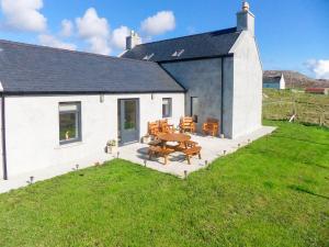 a white building with a patio with a table and chairs at Kilbride Beach Cottage in Pollachar