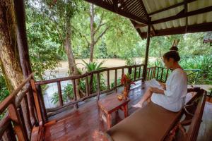 a woman sitting on a bench on a porch at Khao Sok Riverside Cottages in Khao Sok National Park