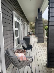 eine Veranda mit zwei Stühlen und einem Stuhl auf einem Haus in der Unterkunft Titoki Grove in Cambridge