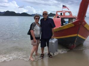 a man and woman standing on the beach next to a boat at Wild Pasir Panjang in Kuah