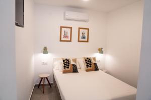 a bedroom with a white bed with pillows and a stool at Hostal Tarantelo Conil in Conil de la Frontera
