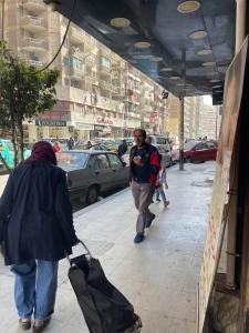 dos personas caminando por una acera con equipaje en شقه مفروشه سوبر لوكس بميامى الاسكندريه en Alexandría