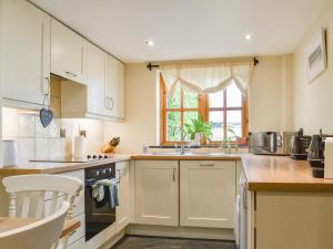 a kitchen with white cabinets and a window at The Tallet Barn in Marhamchurch