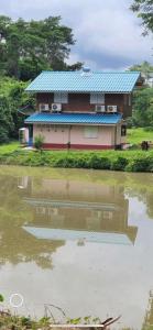 uma casa com um telhado azul ao lado de um corpo de água em นาหินลาดรีสอร์ท Nahinlad Resort em Ban Khok Sawang (2)