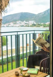una persona sentada en una mesa leyendo un libro en un balcón en Palaia Hotel Datça, en Datça