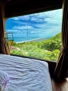a bedroom with a large window looking out at the ocean at Glamping Omah Kayu at Watu Paris Jogja in Girijati