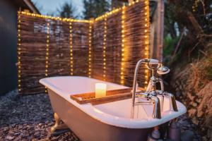 Luxury Glamping Cabin with Outdoor Bath on Cornish Flower Farm في ترورو: حوض استحمام به شمعة وسلسلة من الأضواء