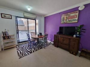 a living room with a table and a tv and purple walls at Little Monica Apartment- Spacious, Affordable & Central in Perth