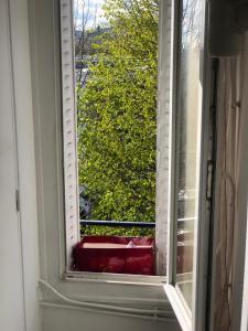 a window with a red couch looking out at a tree at Grand studio aéré entre sol in Montreuil