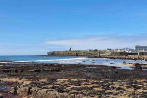 a beach with rocks and the ocean and a lighthouse at Castle View Rooms in Liscannor