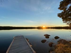a dock in the middle of a lake with the sunset at Cabin 70m from lake. Big garden in Östersund