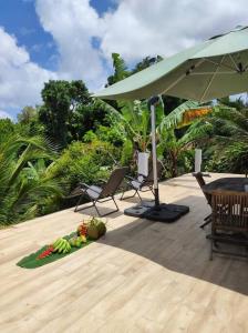 eine Terrasse mit einem Sonnenschirm und Stühlen sowie einer Obstschale in der Unterkunft L'Eucalyptus in La Trinité