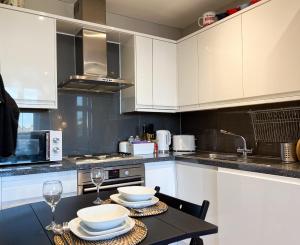 a kitchen with white cabinets and a table with plates and glasses at Stylish 2 Bed Apt - Watford Gen Hospital - Watford FC - Professionals & Contractors Welcome in Watford