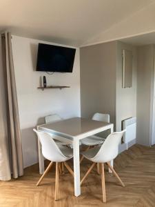mesa de comedor con sillas blancas y TV en la pared en Mobil home 3 chambres mar estang 4 étoiles !, en Canet-en-Roussillon