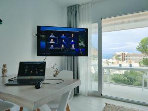 um computador portátil sentado numa mesa com uma televisão na parede em Apartment Formentor with sea view, pool & terrace in Canyamel em Canyamel