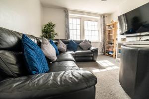 Lovely flat in Crouch End في لندن: أريكة جلدية سوداء مع وسائد زرقاء في غرفة المعيشة