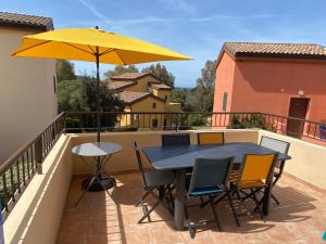 a table and chairs on a balcony with a yellow umbrella at Lozari Beach in Belgodère