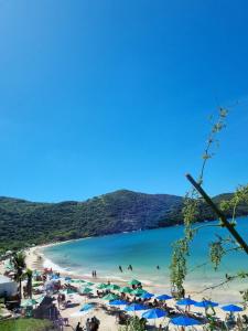 ein Strand mit blauen Sonnenschirmen und Menschen im Wasser in der Unterkunft SANTO MAR HOSTEL in Arraial do Cabo