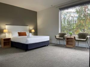a bedroom with a bed and two chairs and a window at Cosmopolitan Hotel Melbourne in Melbourne