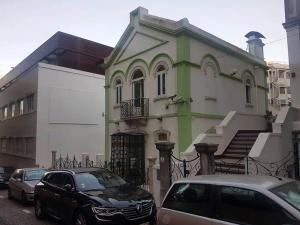 White House Lisbon Hostel في لشبونة: بيت اخضر وبيضاء فيه سيارات تقف امامه